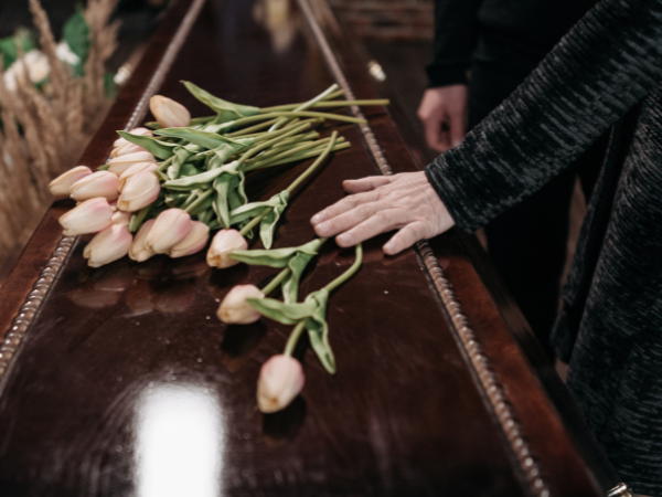 Funeral service with a man putting his hand on a coffin adorned with flowers